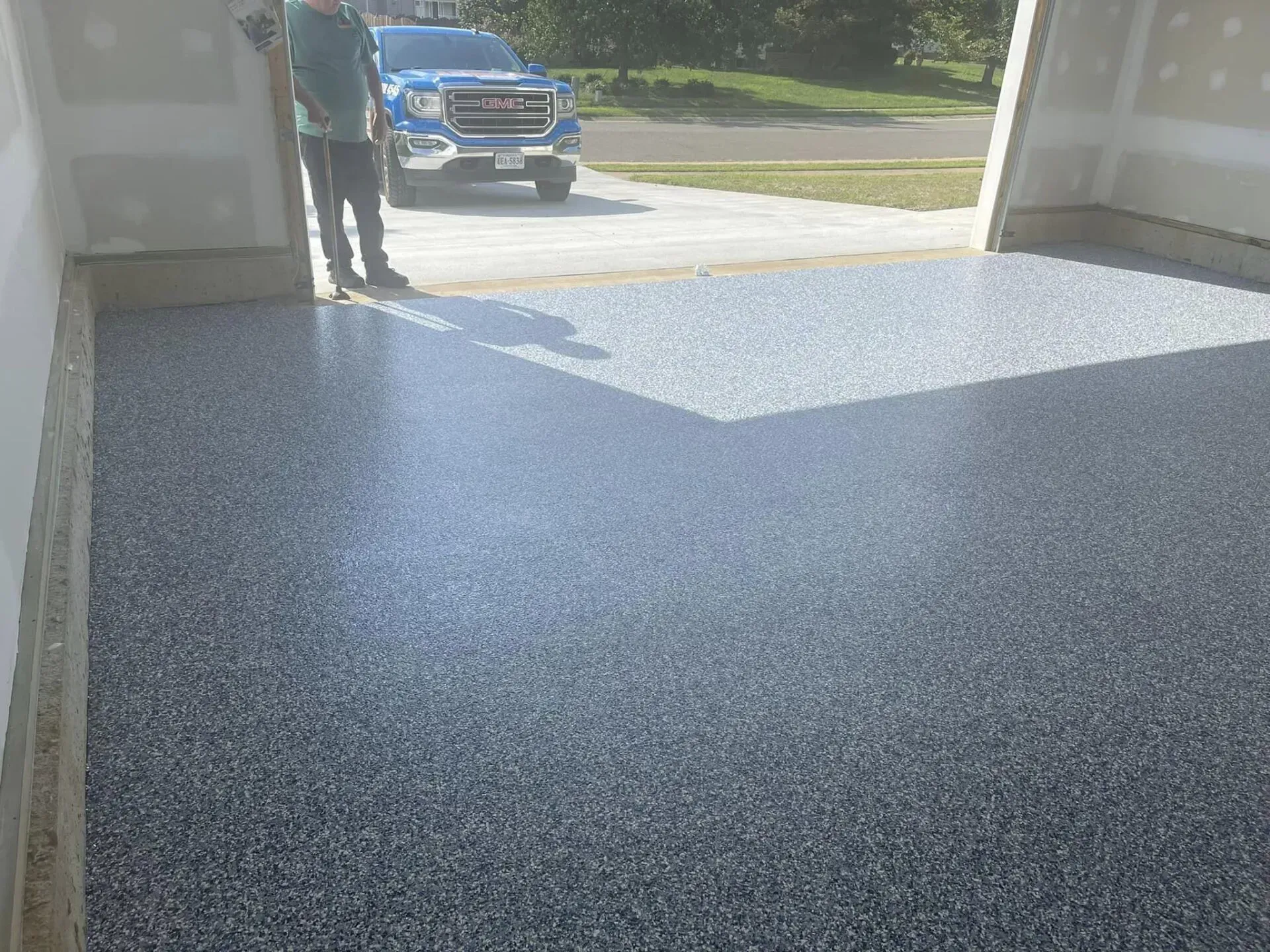 Blue pickup truck parked in a garage doorway with a person standing nearby on the left.