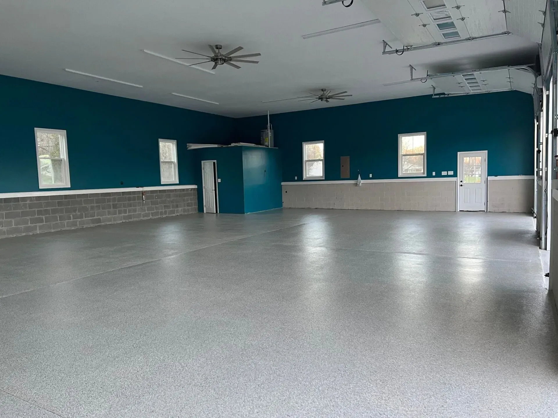 Empty indoor hall with teal walls, gray floor, and windows along the far wall