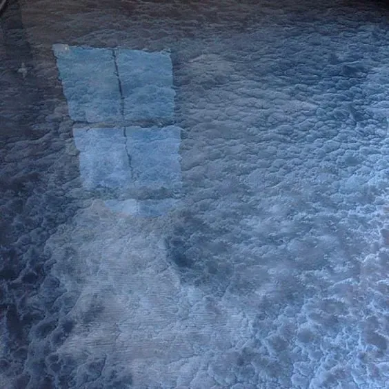 Blue-tinted frothy water or ice with a faint window reflection near the top left