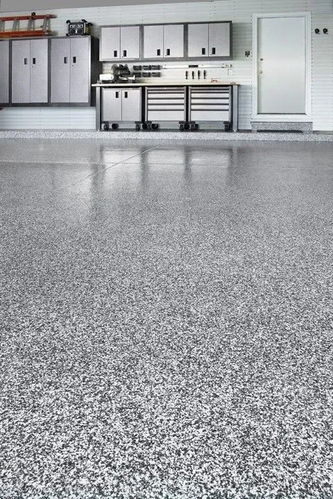 Empty garage with gray speckled floor and white cabinets along the back wall