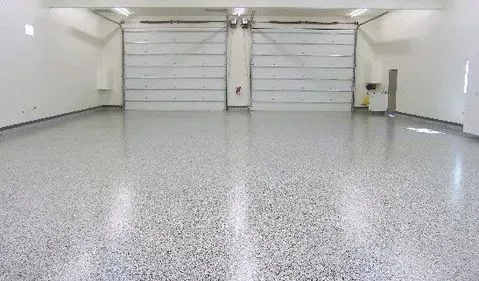 Empty garage with white walls, two closed garage doors, and a speckled gray epoxy floor.