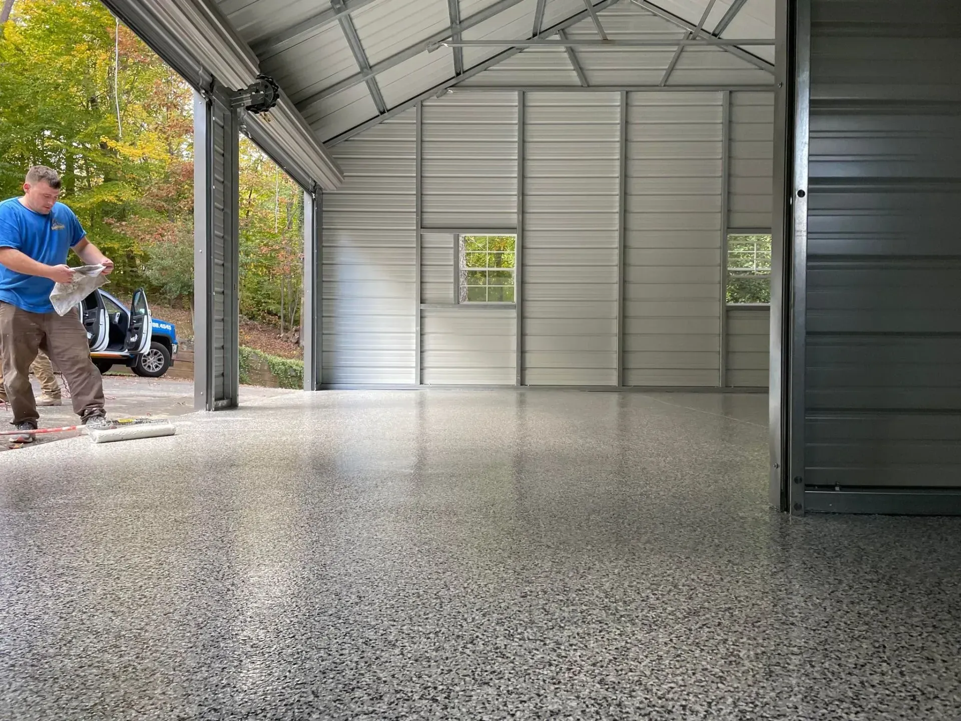 Spacious metal workshop interior with a speckled floor; a person stands near the open doorway outside.