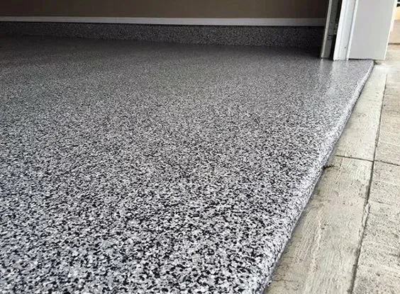 Speckled gray epoxy garage floor beside a white wall and concrete driveway edge