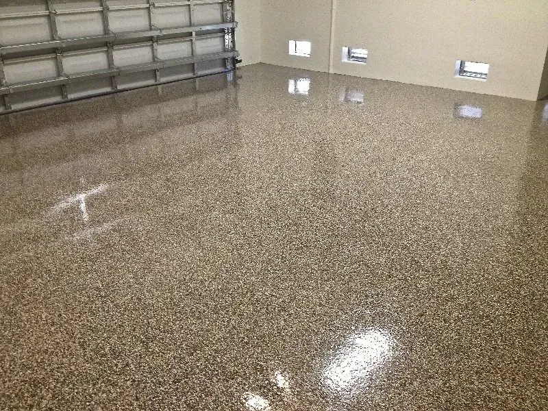 Empty garage with glossy brown speckled epoxy floor and closed metal door.