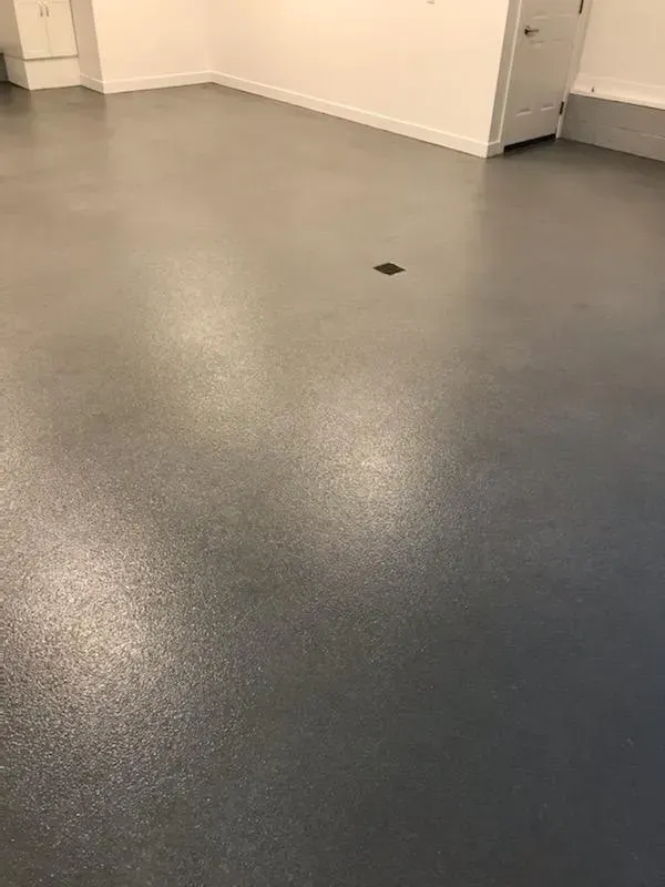 Empty gray floor in a sparse indoor room with white walls and a small floor drain.