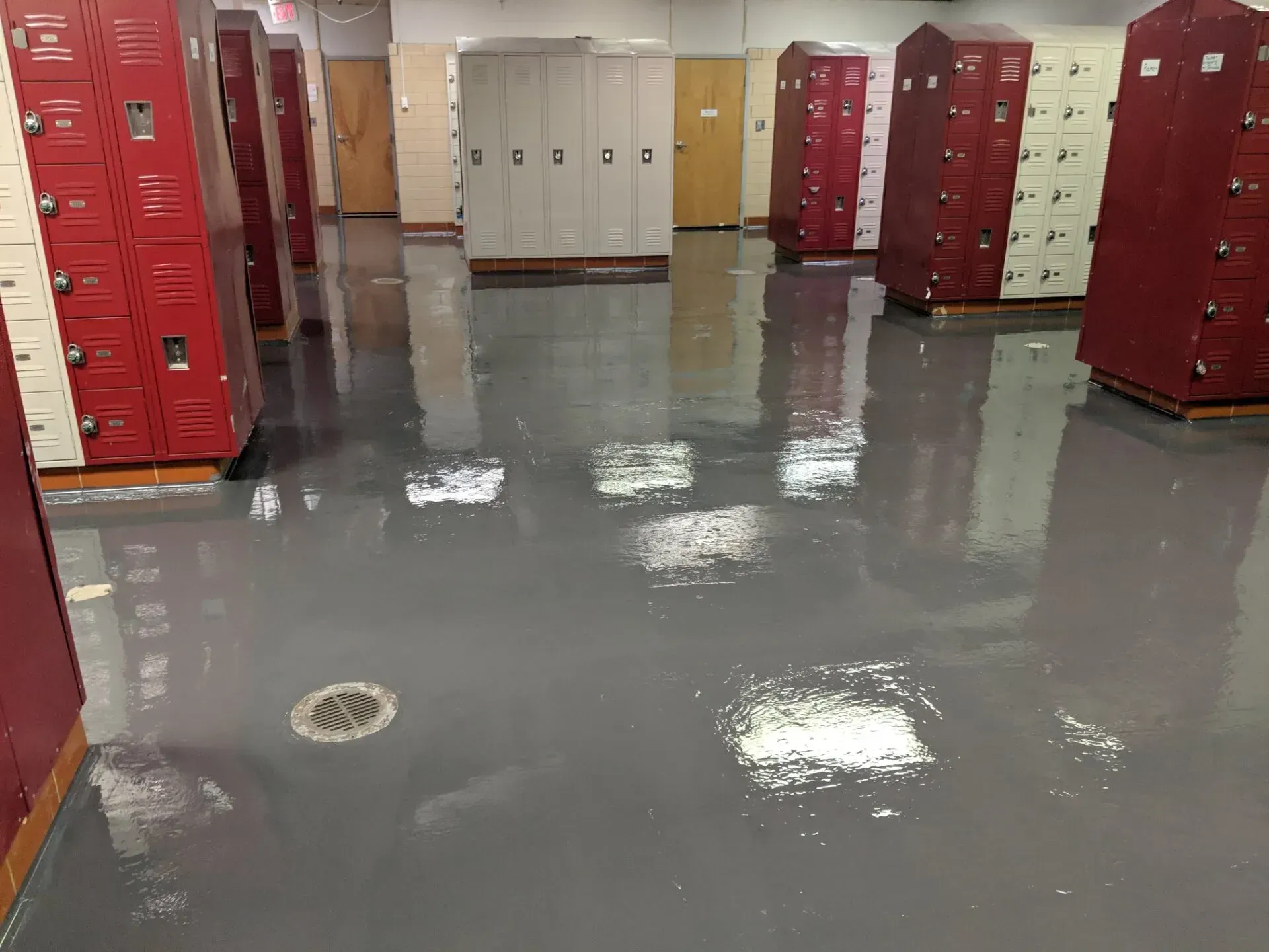 Locker room with red and beige lockers and a wet, glossy floor reflecting the lights.