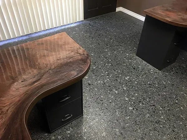 Office corner with two wood-top desks and black pedestals on a speckled carpet floor