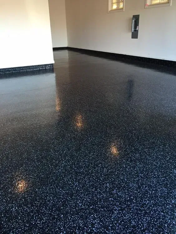 Empty glossy black-speckled floor in a bright room with beige walls and windows.