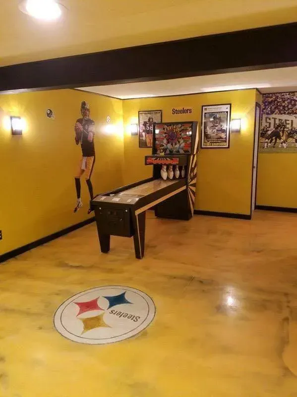 Yellow game room with a foosball table, wall murals, and a floor logo near the center.