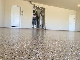 Empty garage with speckled concrete floor, white doors, and storage water heater in the back.