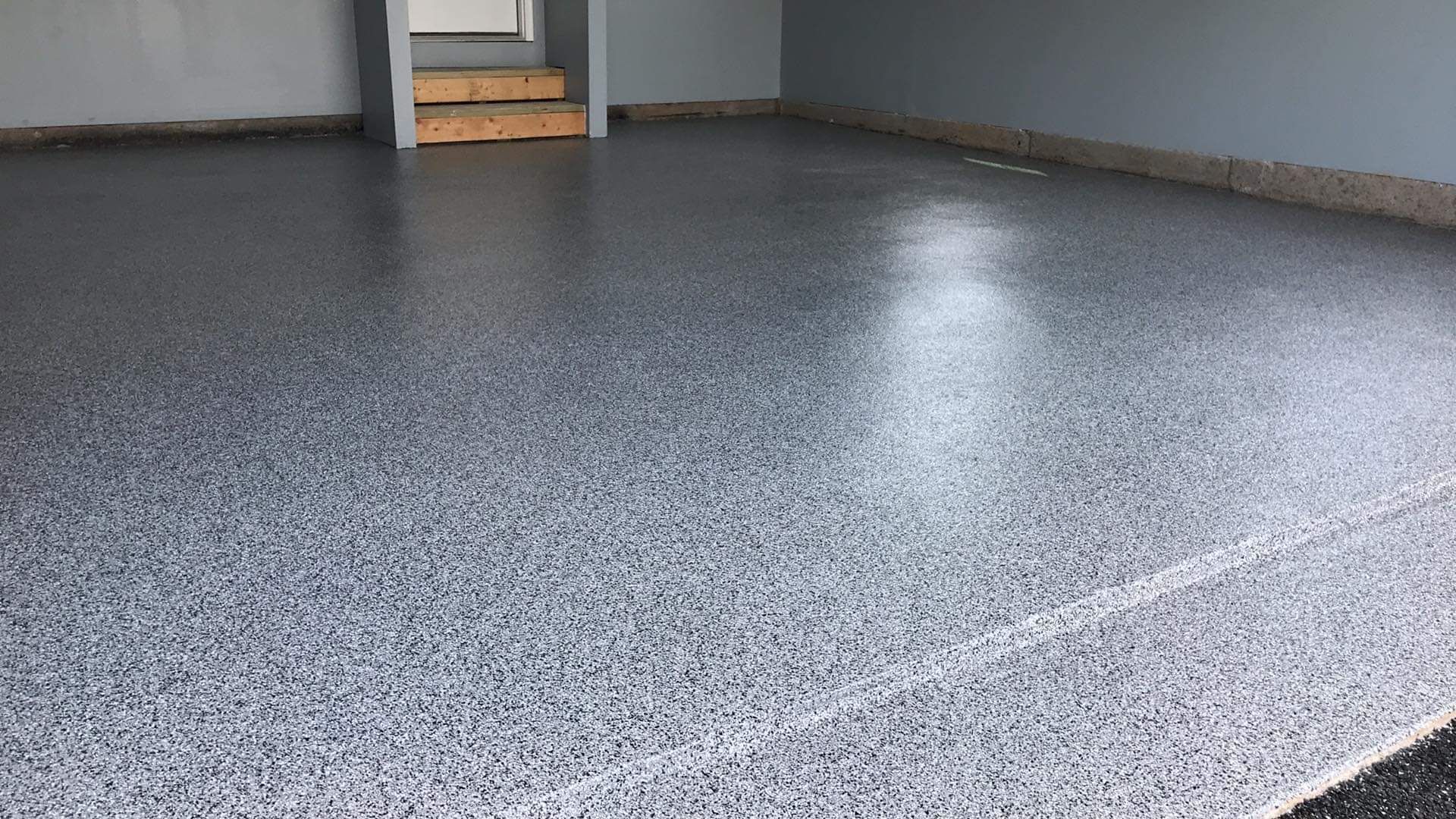 Empty gray speckled floor in a room with a doorway in the background