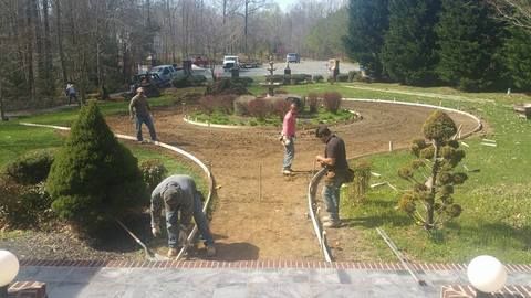 People landscaping a circular garden with fresh soil, plants, and tools on a sunny day.