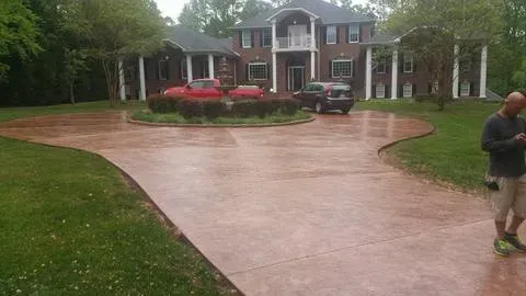 Wet driveway leading to a large brick house with red cars and a person standing on the right side