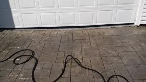 Hose on a paved driveway in front of a white garage door