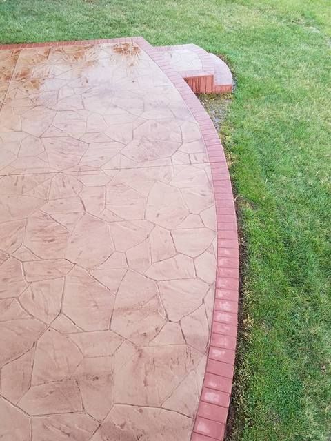 Curved brick-edged stone patio beside green grass lawn