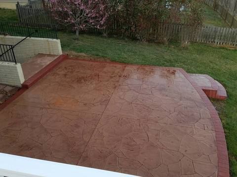 Red stamped concrete patio beside a grassy backyard and fence.