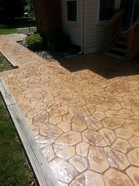 Stamped concrete patio beside a house, with a tan stone pattern in bright sunlight.
