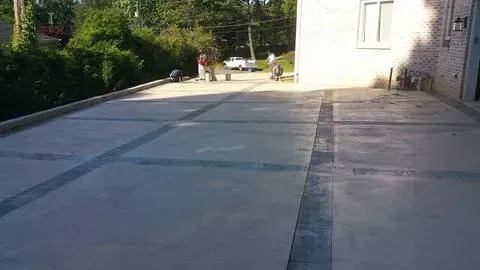 Empty concrete driveway beside a white building, with trees and a few people in the distance
