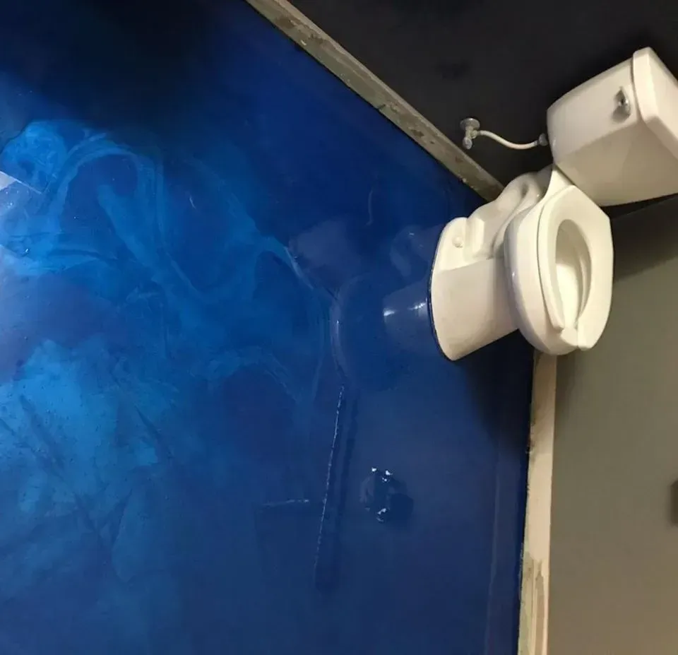 Blue painted wall with a white wall-mounted toilet and tank in a corner, viewed at an angle