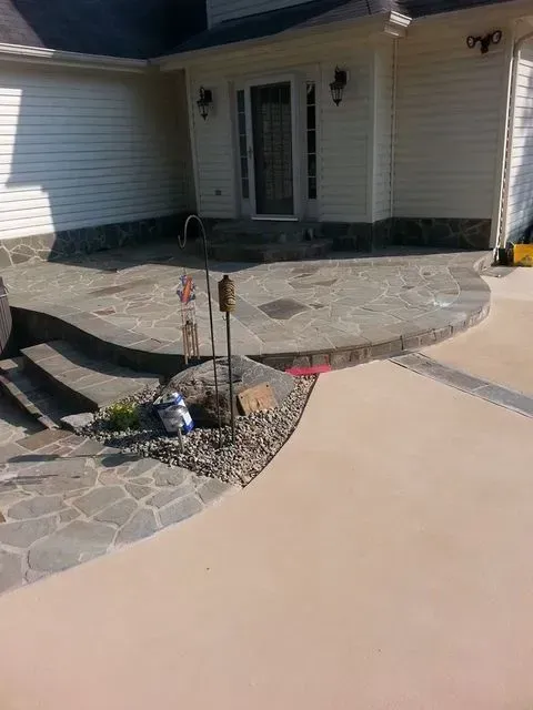 Front entrance with stone porch, curved concrete walkway, and small garden border in sunlight