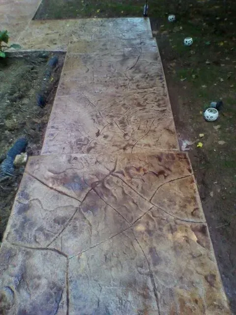 Stamped concrete walkway leading through a yard, bordered by grass and small scattered items.