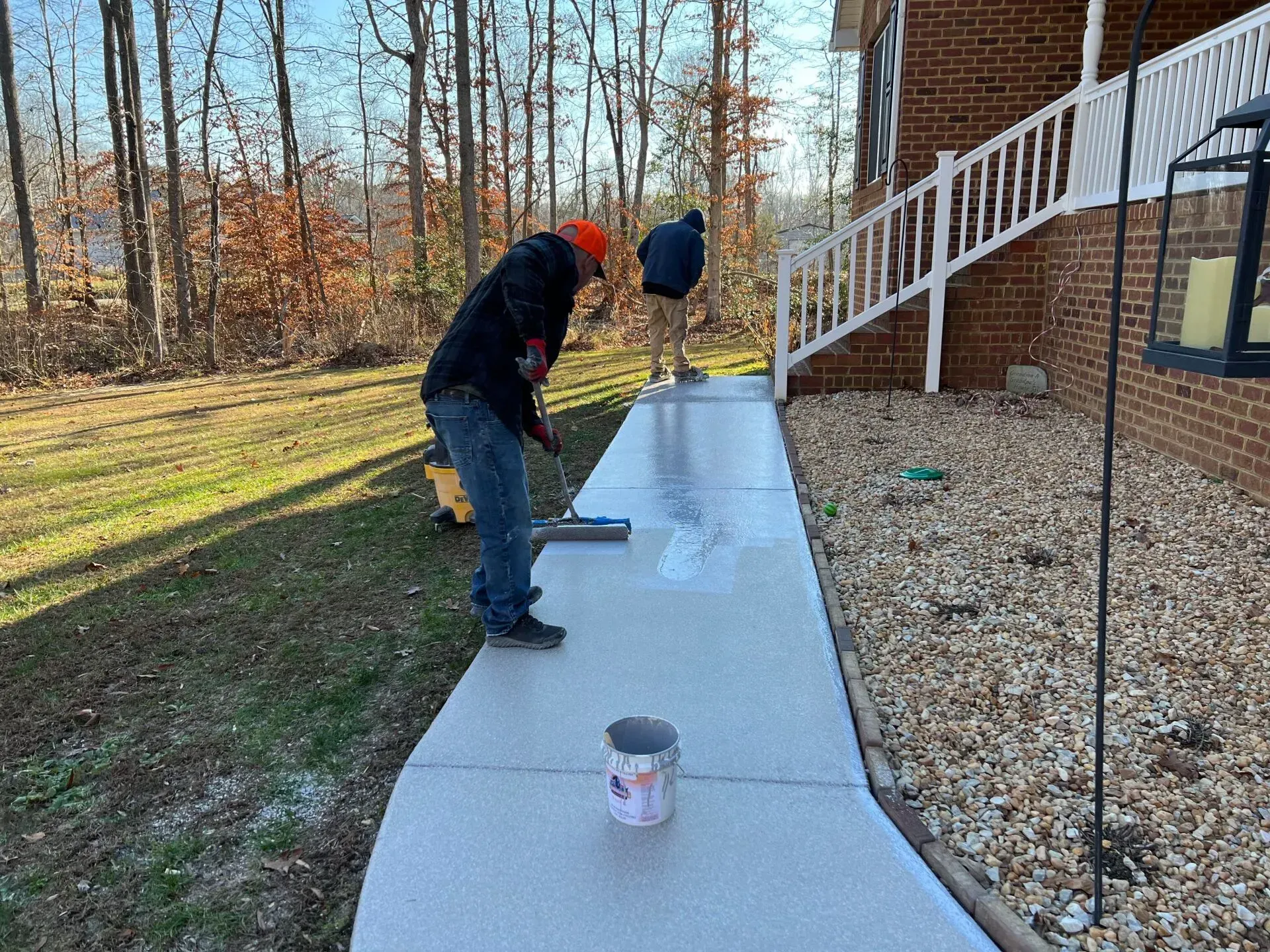 Two people painting a long concrete walkway beside a house in a yard