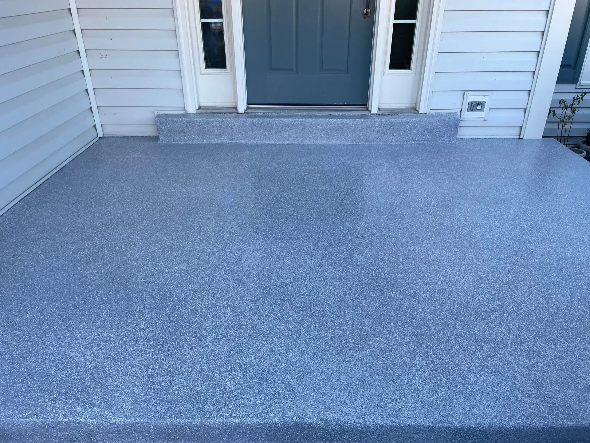 Front porch with blue-gray concrete coating leading to a gray front door and white siding.