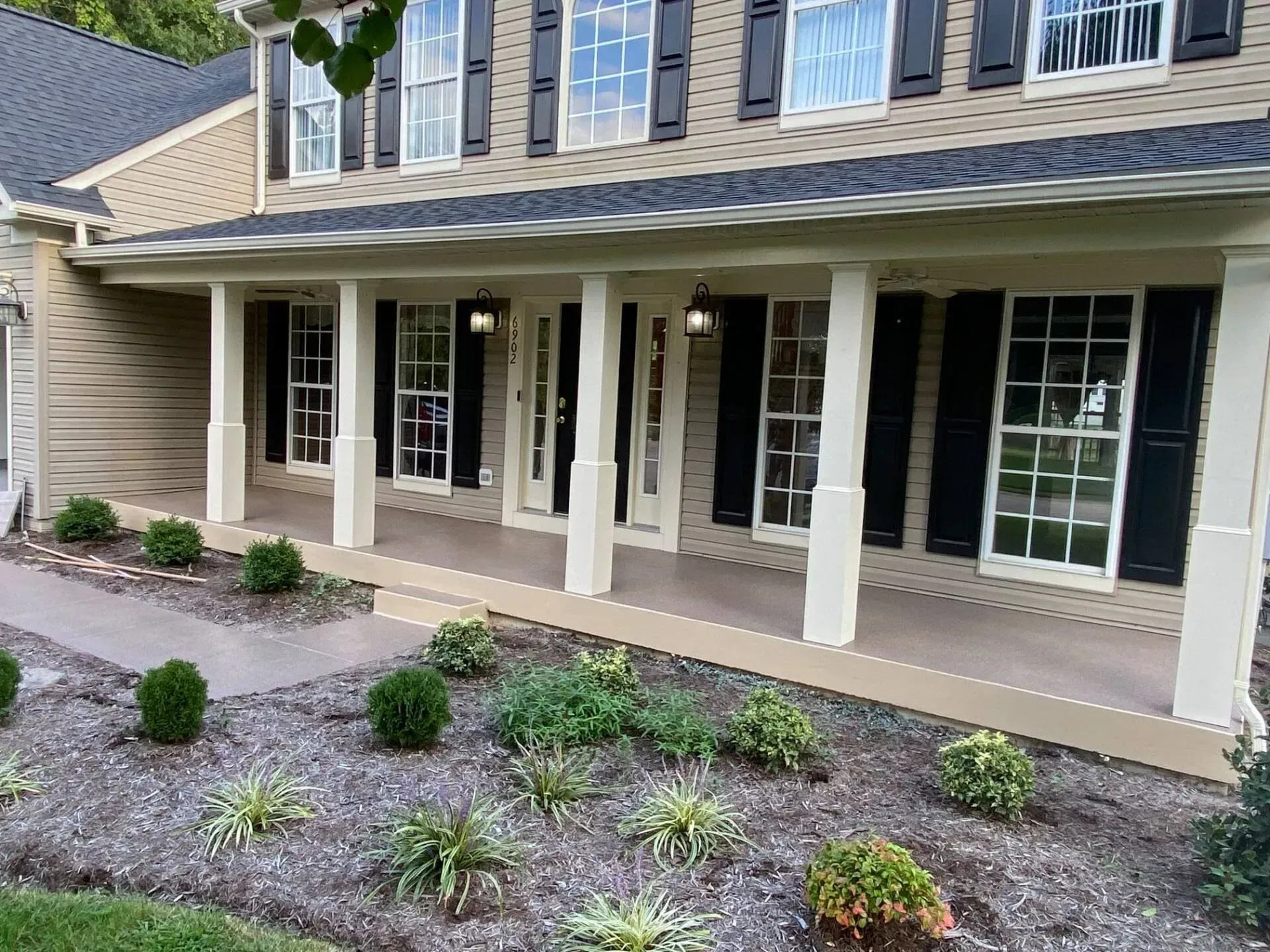 Front porch of a house with beige columns, dark siding, and a landscaped gravel garden in front