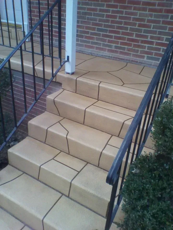 Outdoor brick steps with tan tile treads and black railings beside a brick wall
