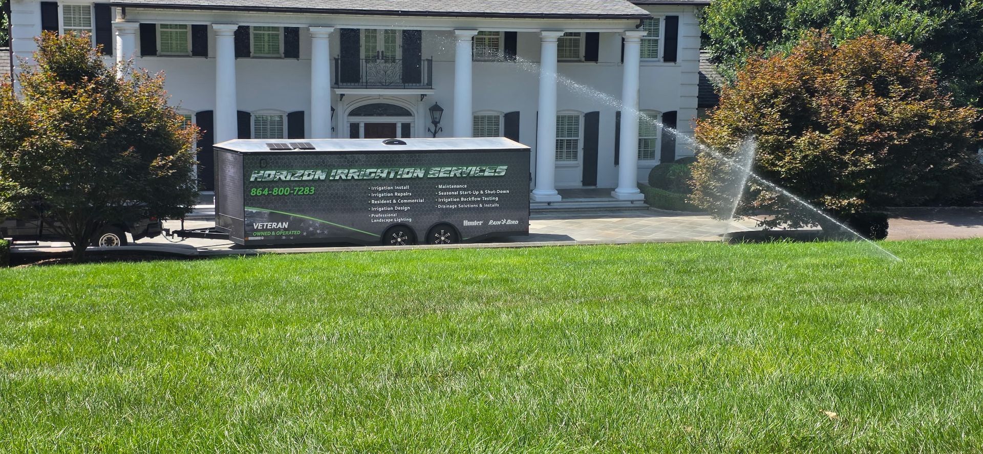 White house with porch and a green advertising truck parked on the lawn in front