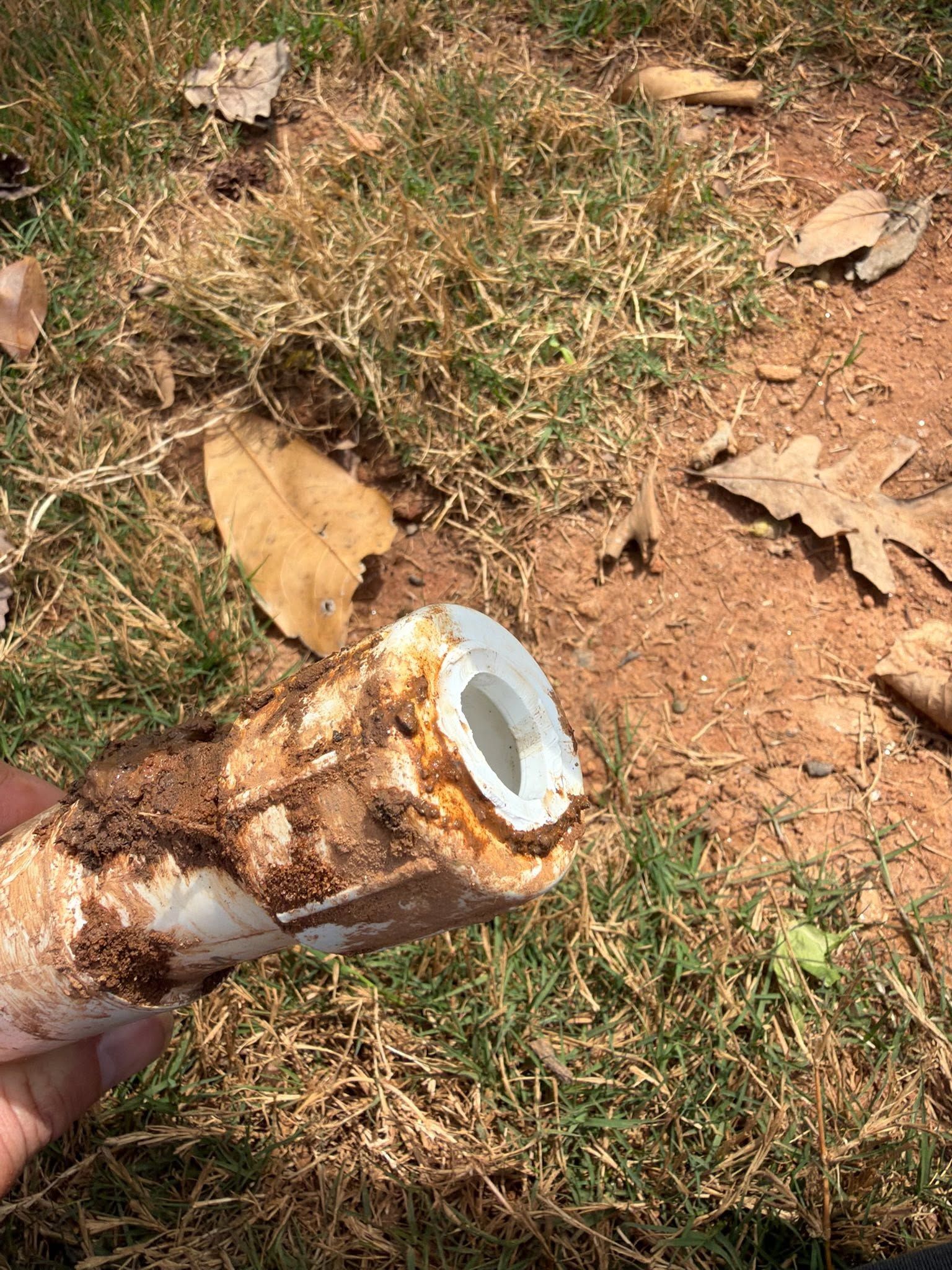 Broken pipe with rusted end held over dry grass and dirt ground