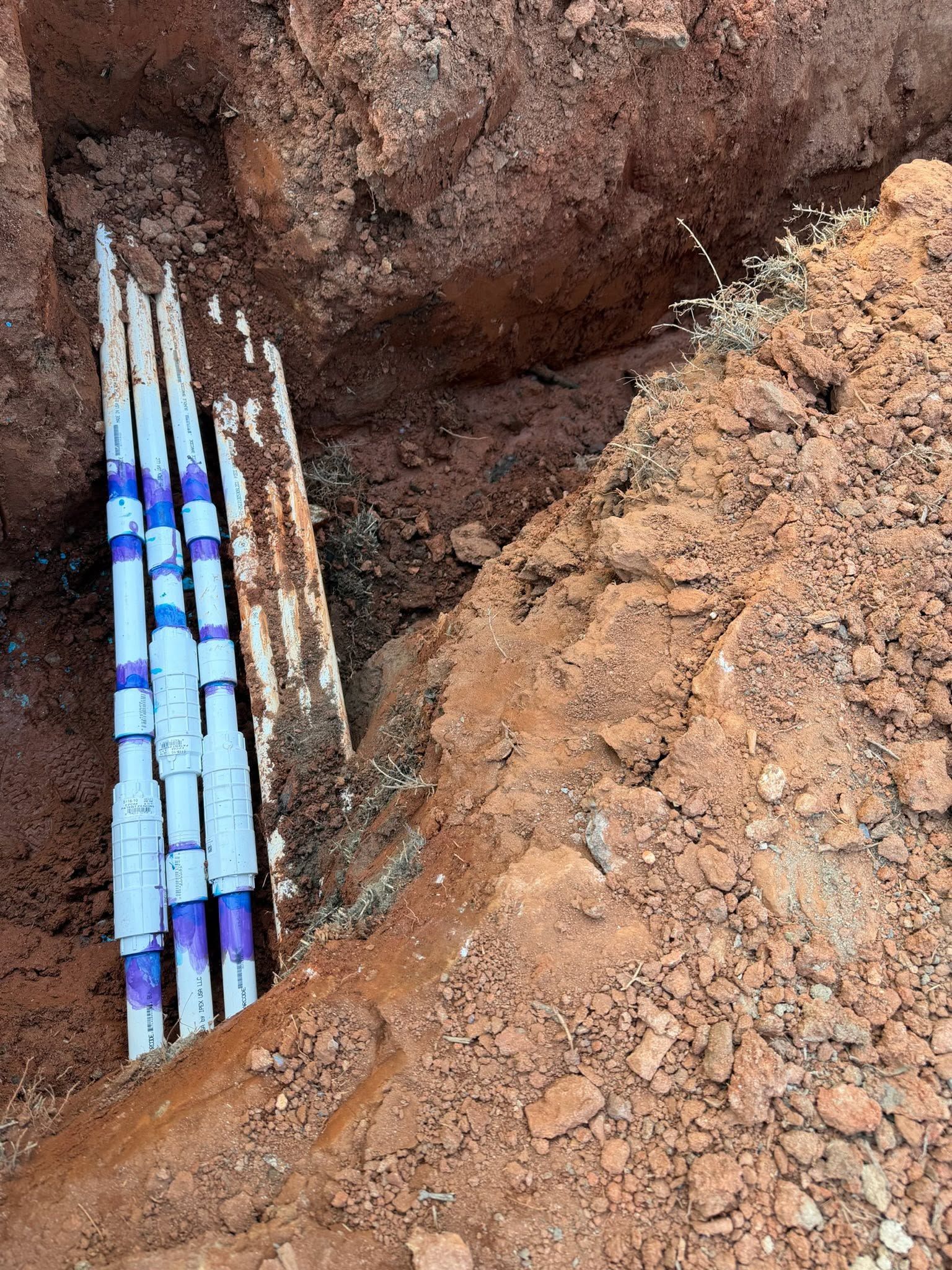 Exposed blue utility pipes in a dirt trench during excavation work