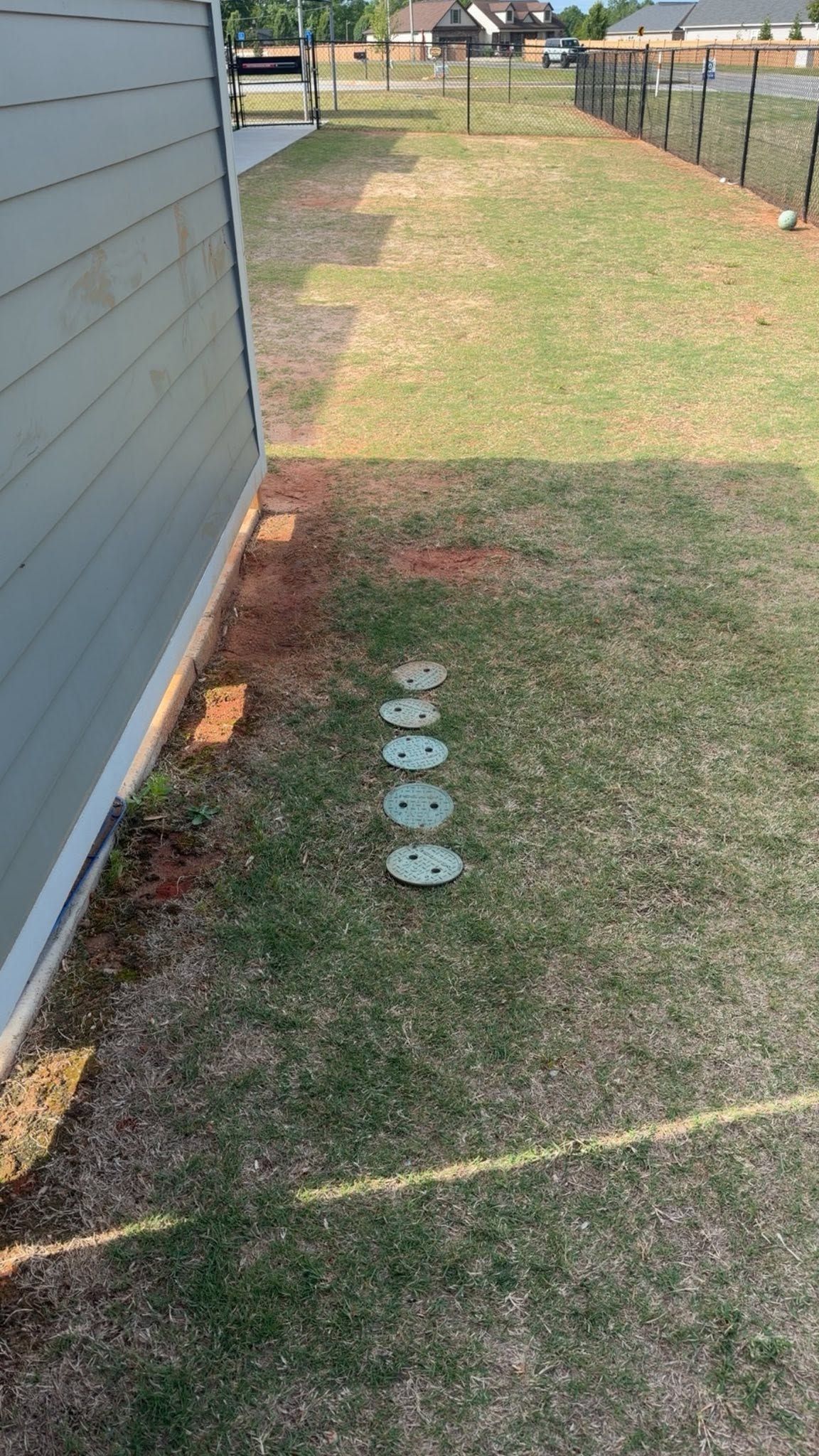 Backyard side yard with a row of round stepping stones beside a gray house and fence.