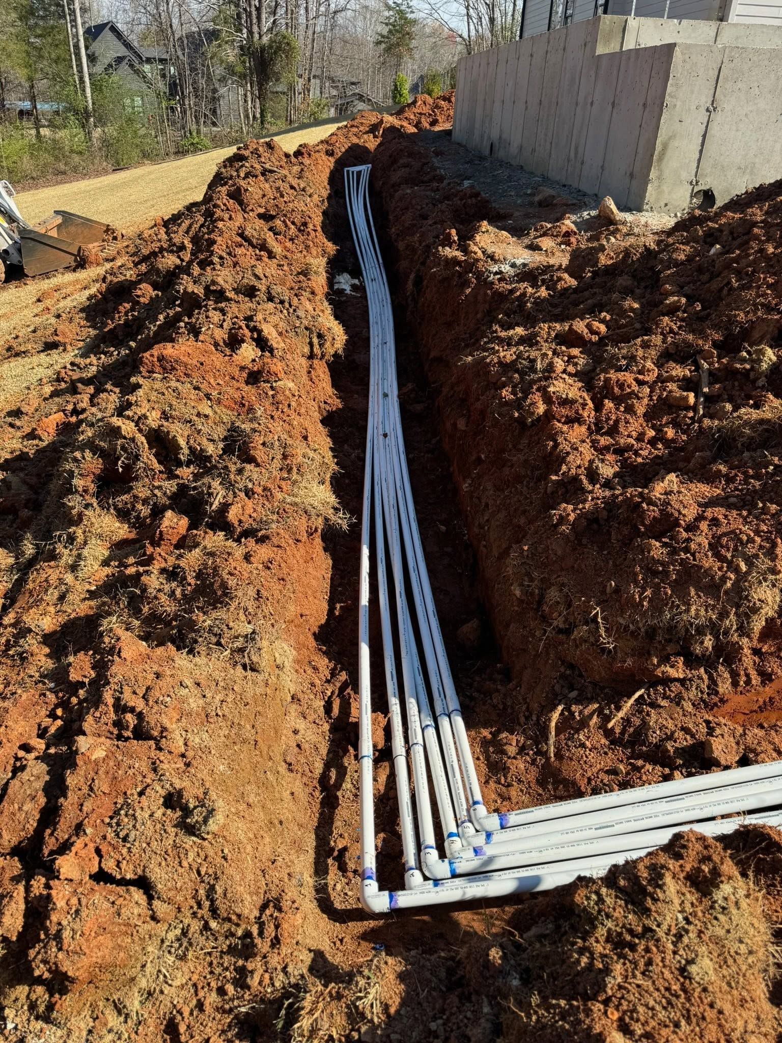 PVC pipes laid in a trench beside a concrete wall on a dirt construction site
