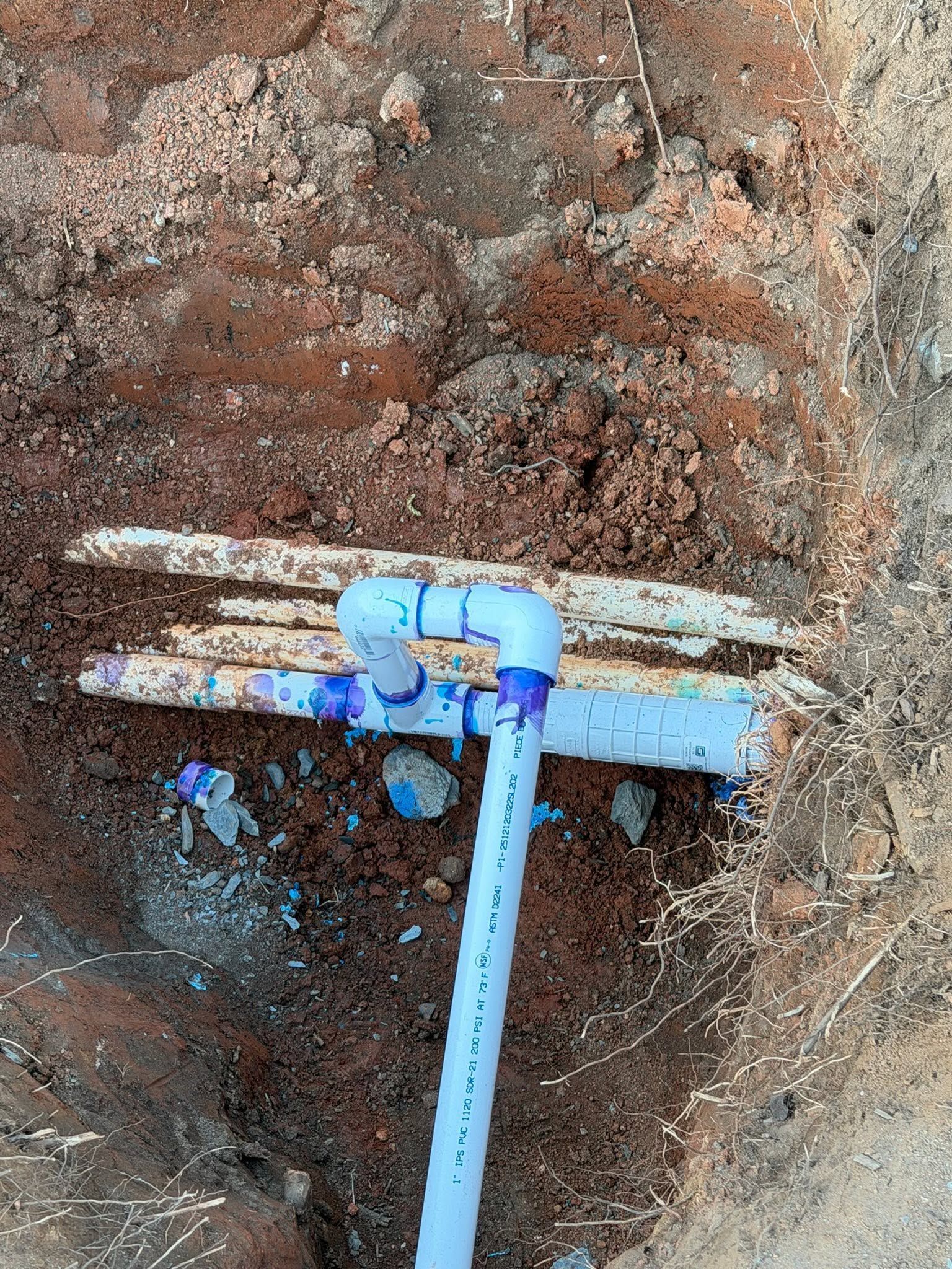 Blue PVC pipe and valve exposed in a muddy excavation hole in the ground