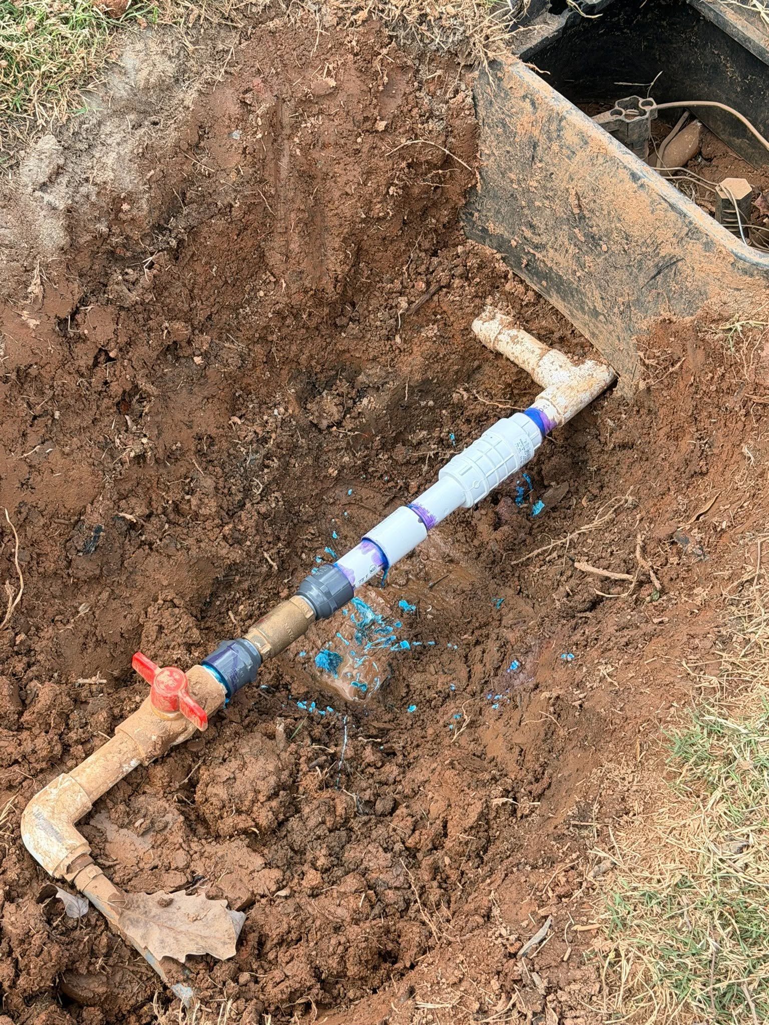 Pipe assembly lying in a dirt trench with blue tape and red valve handle