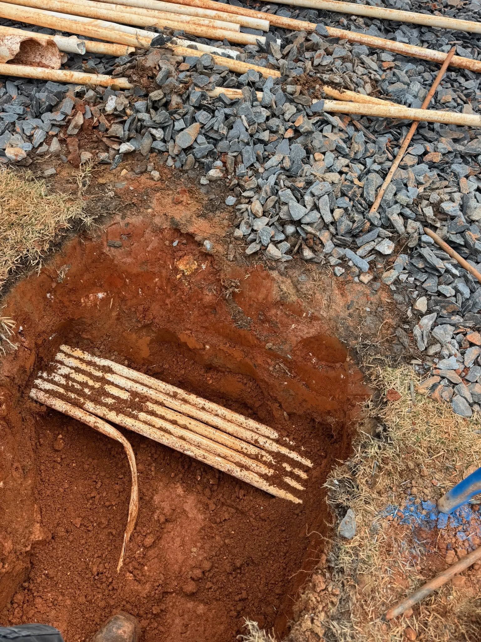 Construction site with exposed red soil, gravel, and wooden rebar supports in a dug-out trench