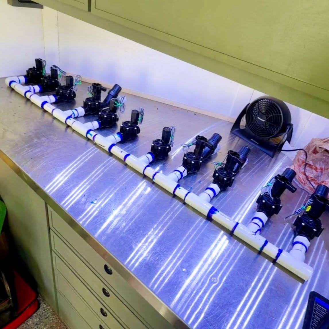Row of small black sensors mounted on a white PVC pipe on a workbench, with a fan at the end.