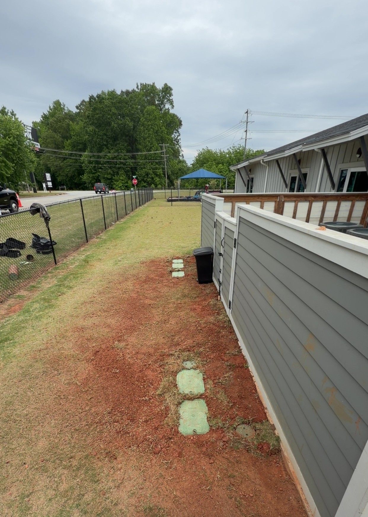Backyard beside a gray house, with a gravel path, stepping stones, fence, and cloudy sky