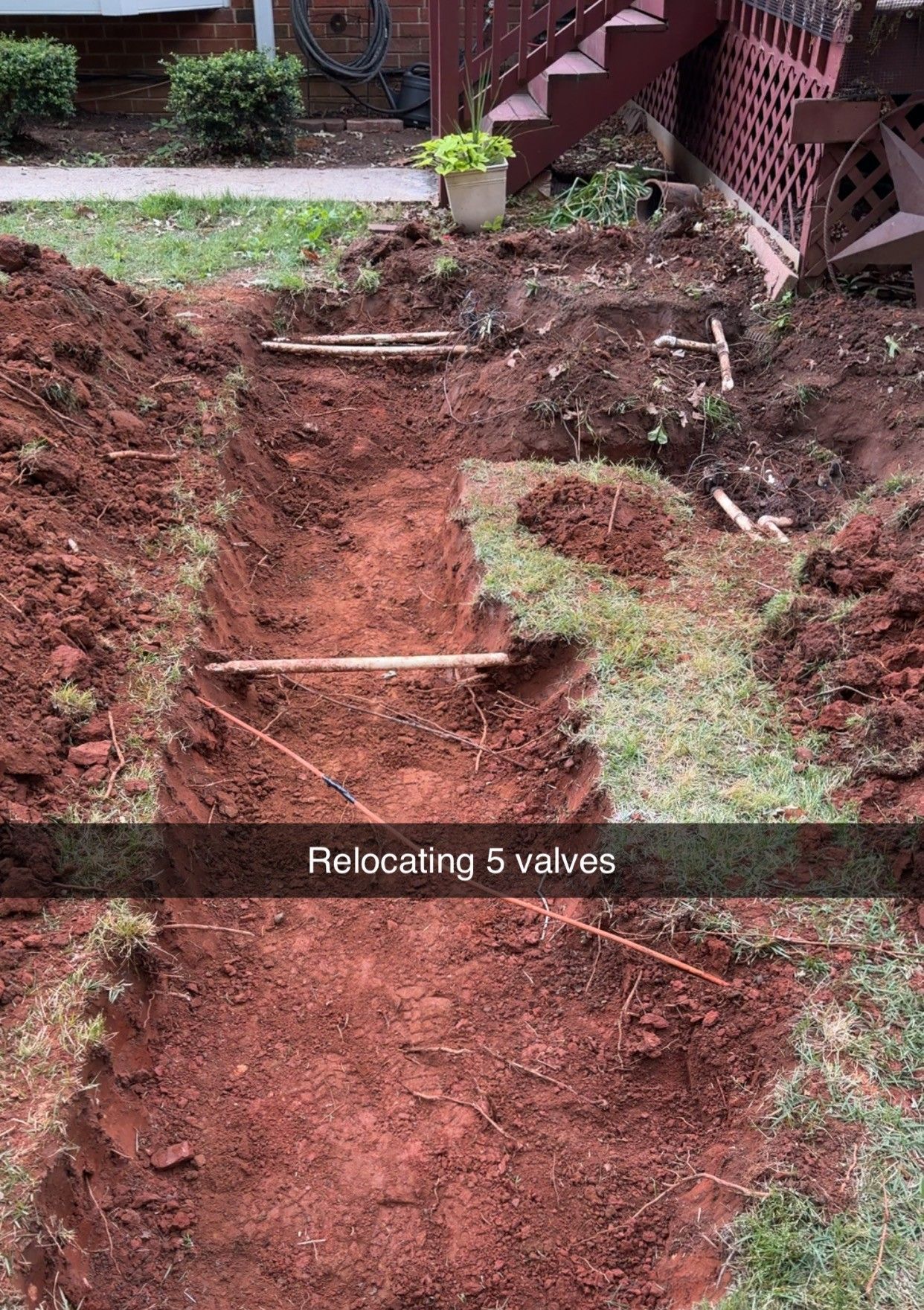 Backyard trench being dug beside a house, with overlay text reading “Relocating 5 valves.”