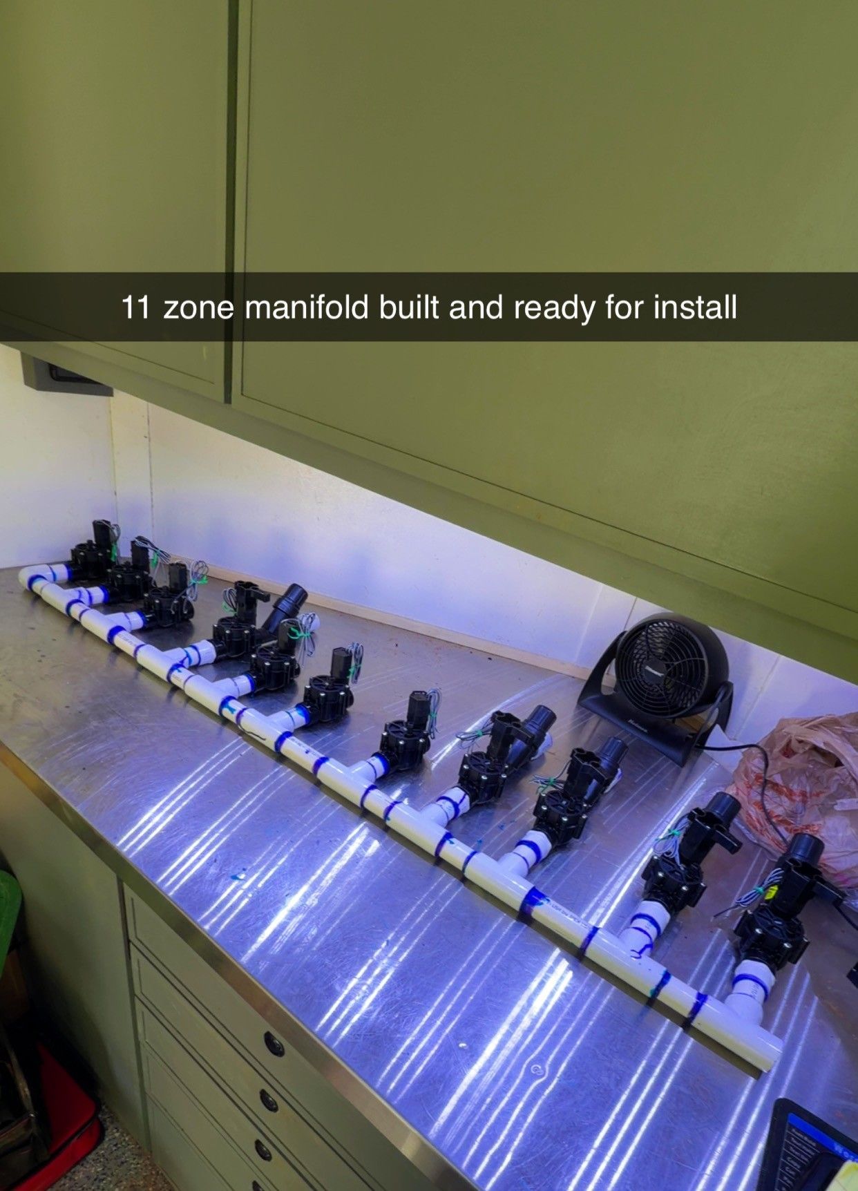 Row of small devices on a lit shelf under cabinets, with text reading “11 zones manifold sold and ready for install”
