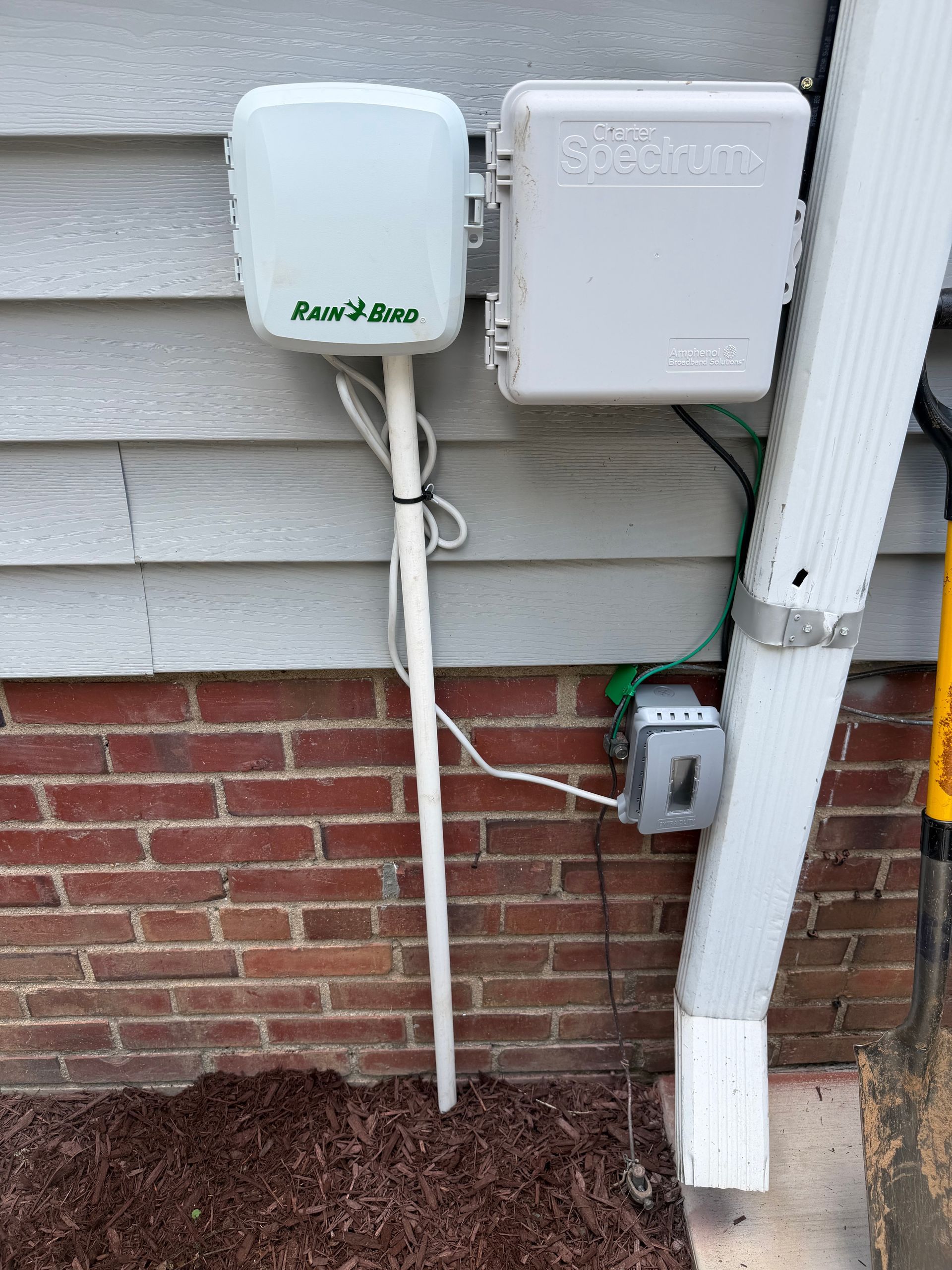 Outdoor utility boxes and cables mounted on a house wall beside a downspout.