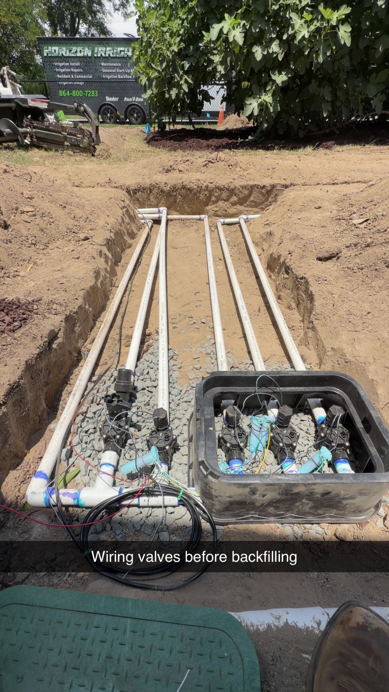 Irrigation pipes run through a dirt trench to a small water-filled basin in a field.