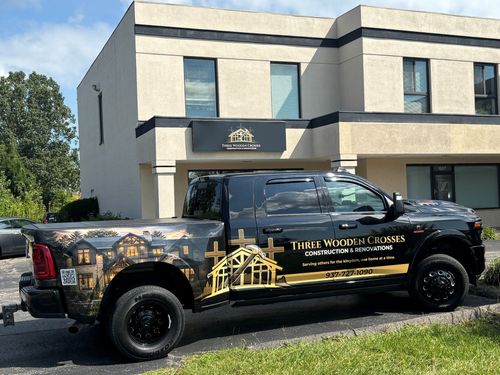 Black pickup truck with gold graphics parked outside a beige building.
