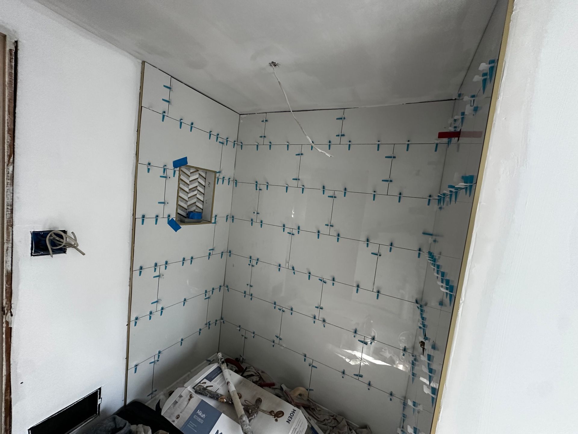 Small unfinished bathroom under renovation, with tiled walls and construction debris on the floor.