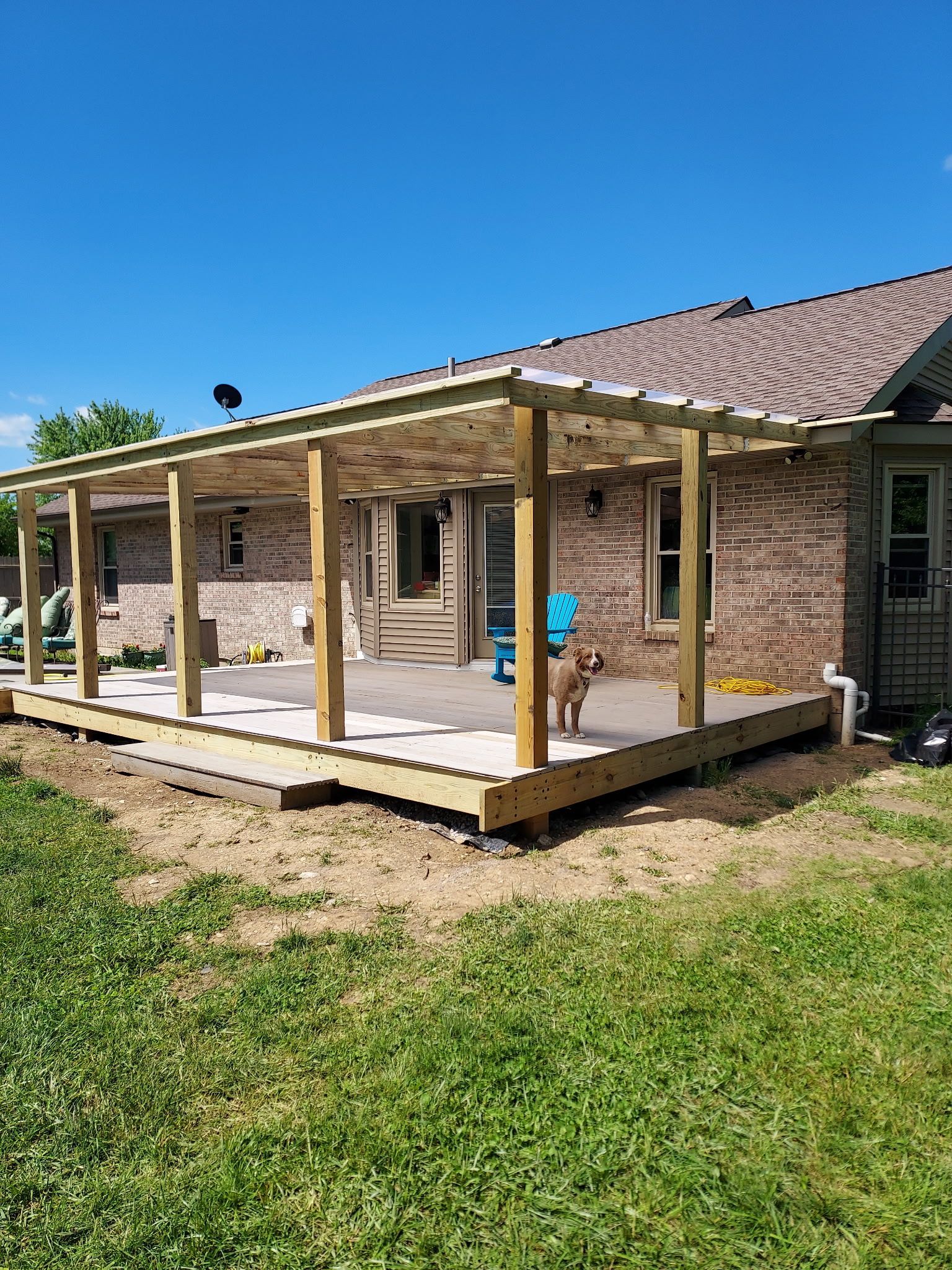 Backyard deck under construction with wooden posts and railings beside a brick house.