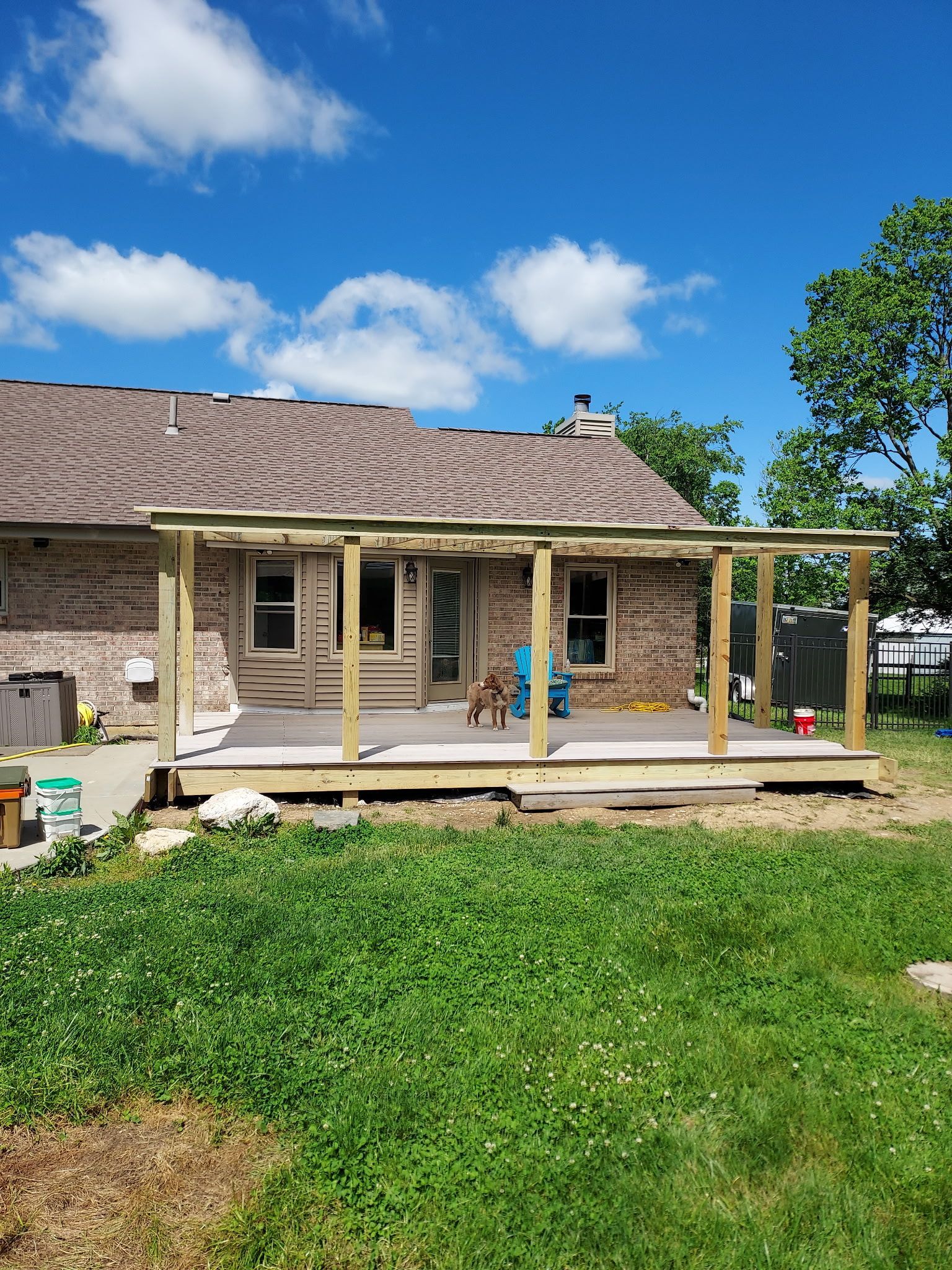 Stone house with a front porch, two people standing outside, and a grassy yard under a blue sky
