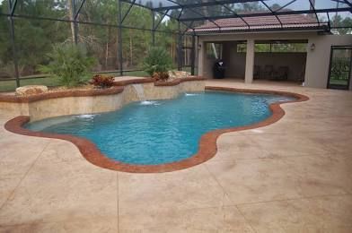 Covered backyard pool with tan deck, stone edging, and screened enclosure.