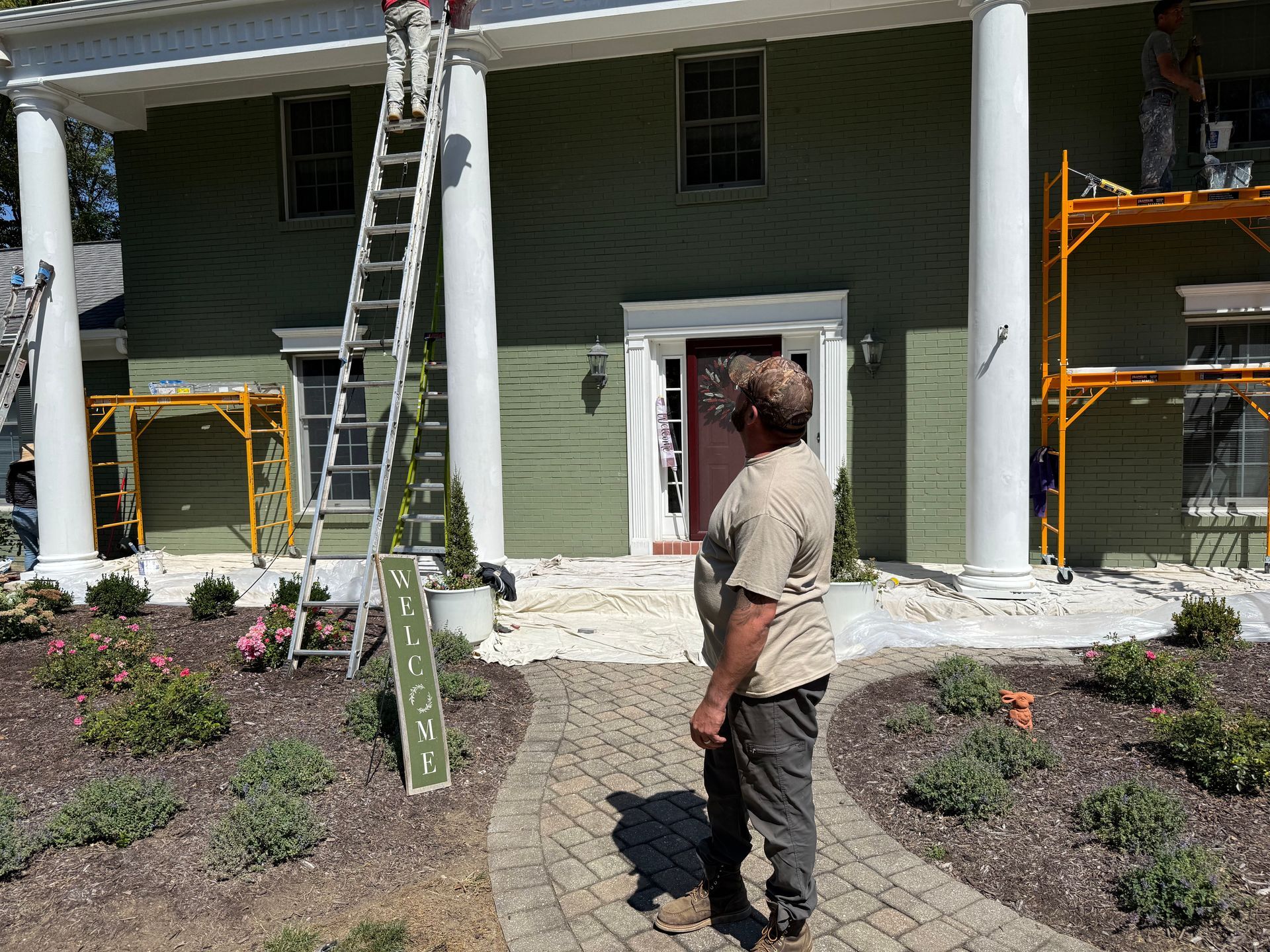 Worker standing in front of a house with ladders and scaffolding during exterior painting work