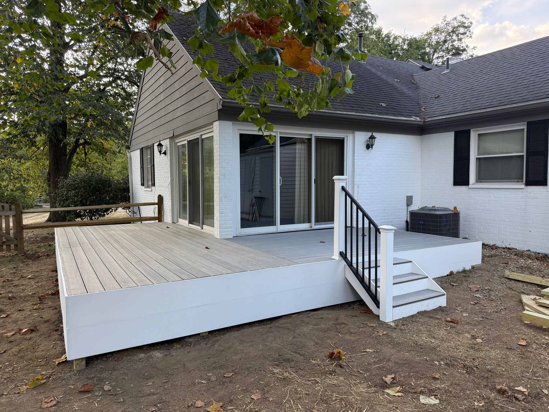 White house with a large wooden deck and steps leading to a sliding glass door.